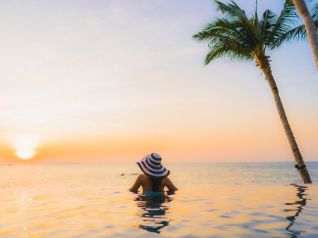 Woman entering the sea with a white hat with black horizontal stripes and a palm tree beside